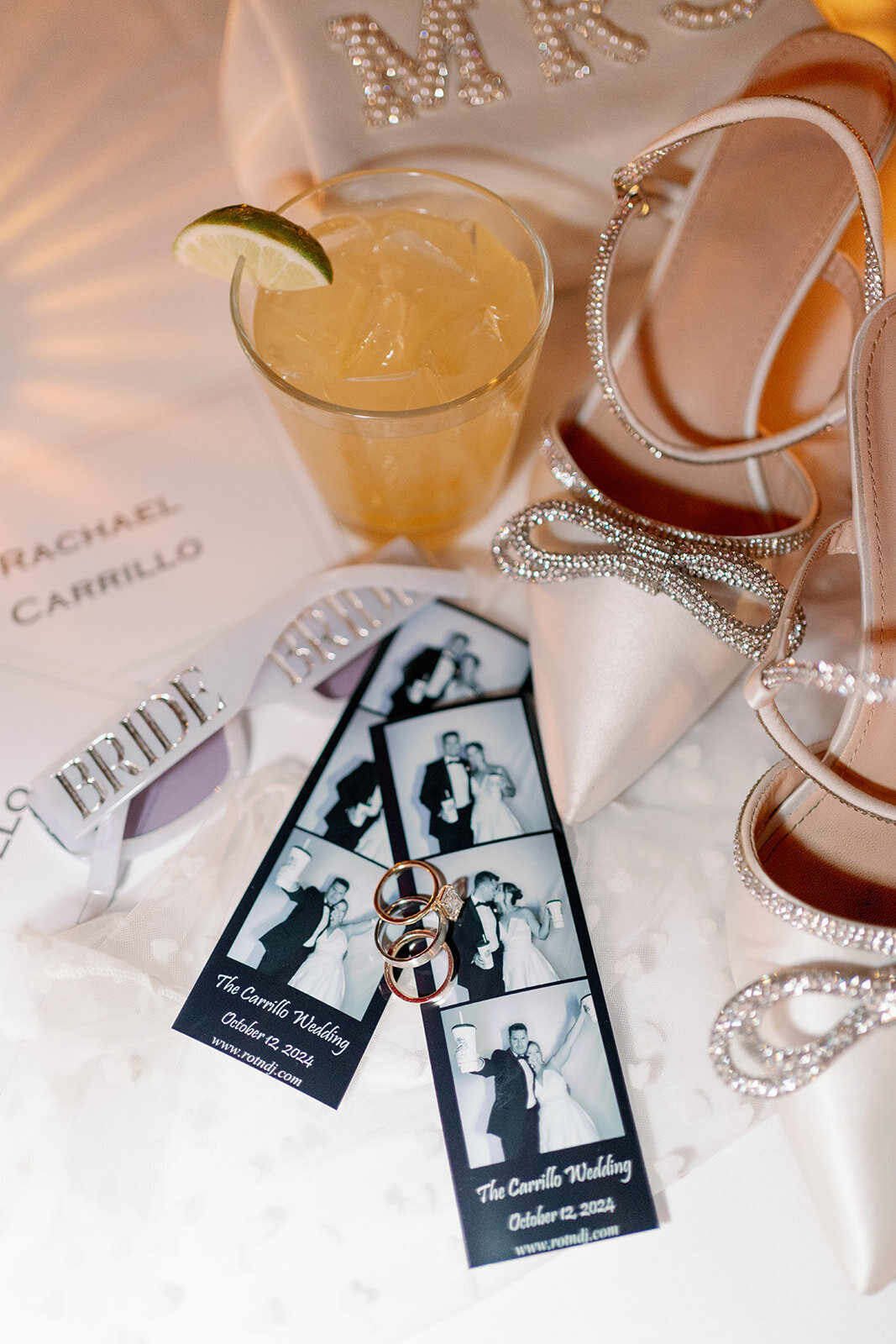 A photo of the couples glasses, rings, polaroid strip, and cocktail 