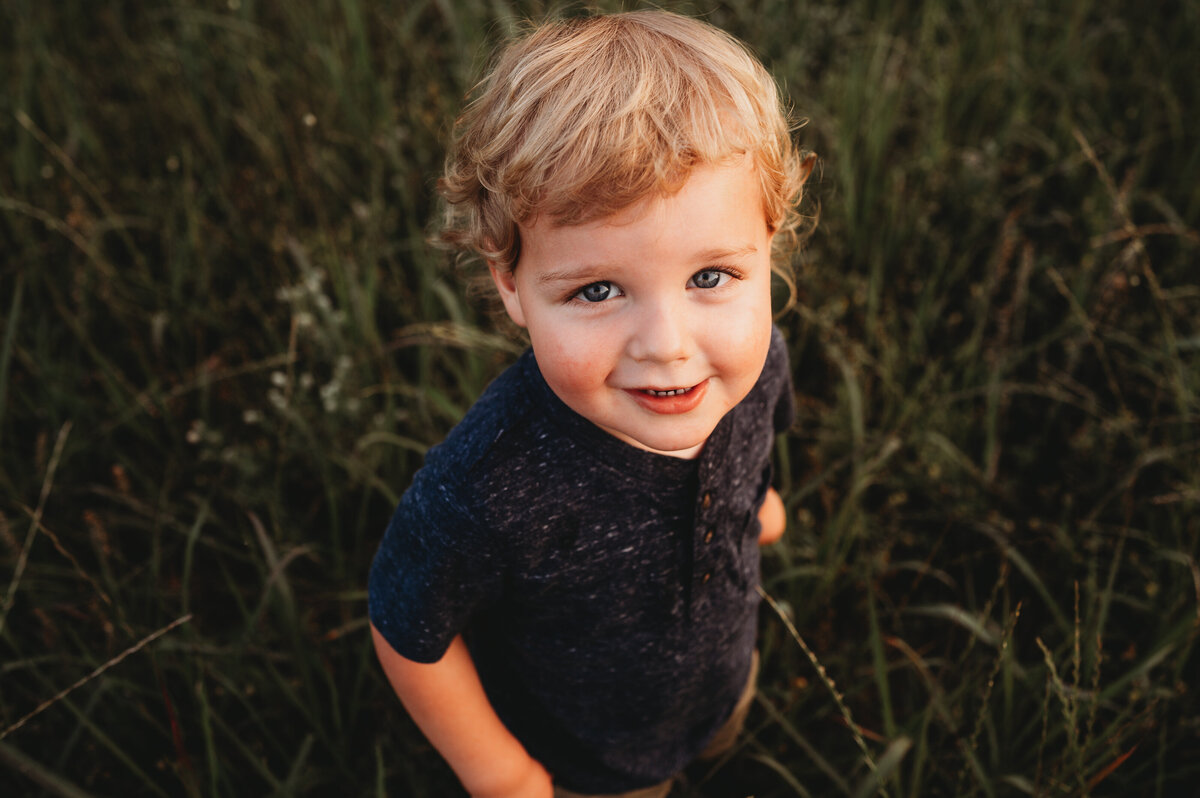 little blonde boy plays and smiles during family photos in an open field