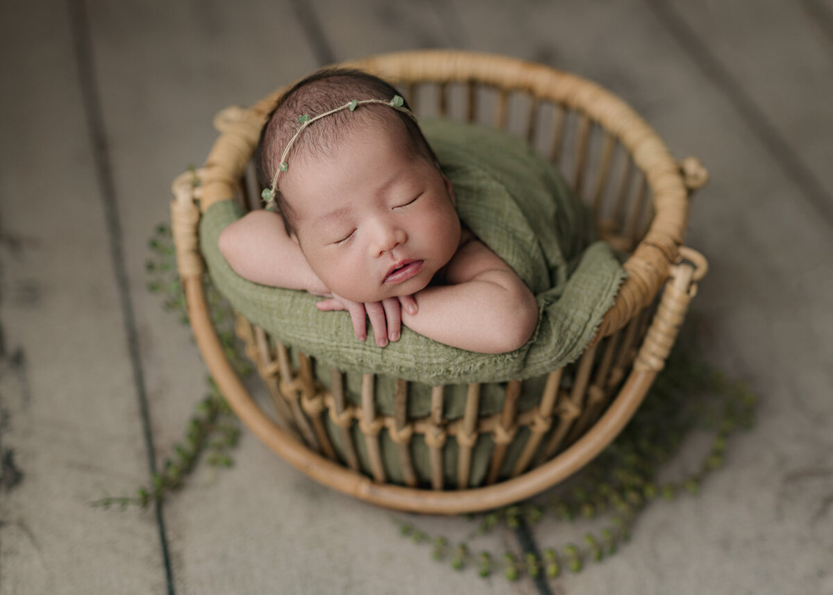 baby in green basket laying on hands