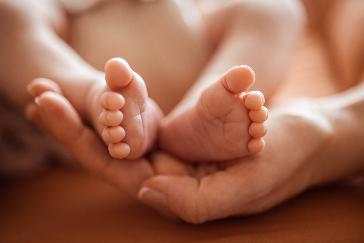 Livsstilsfoto nærbilde av babyens føtter holdt i en mors hånd.