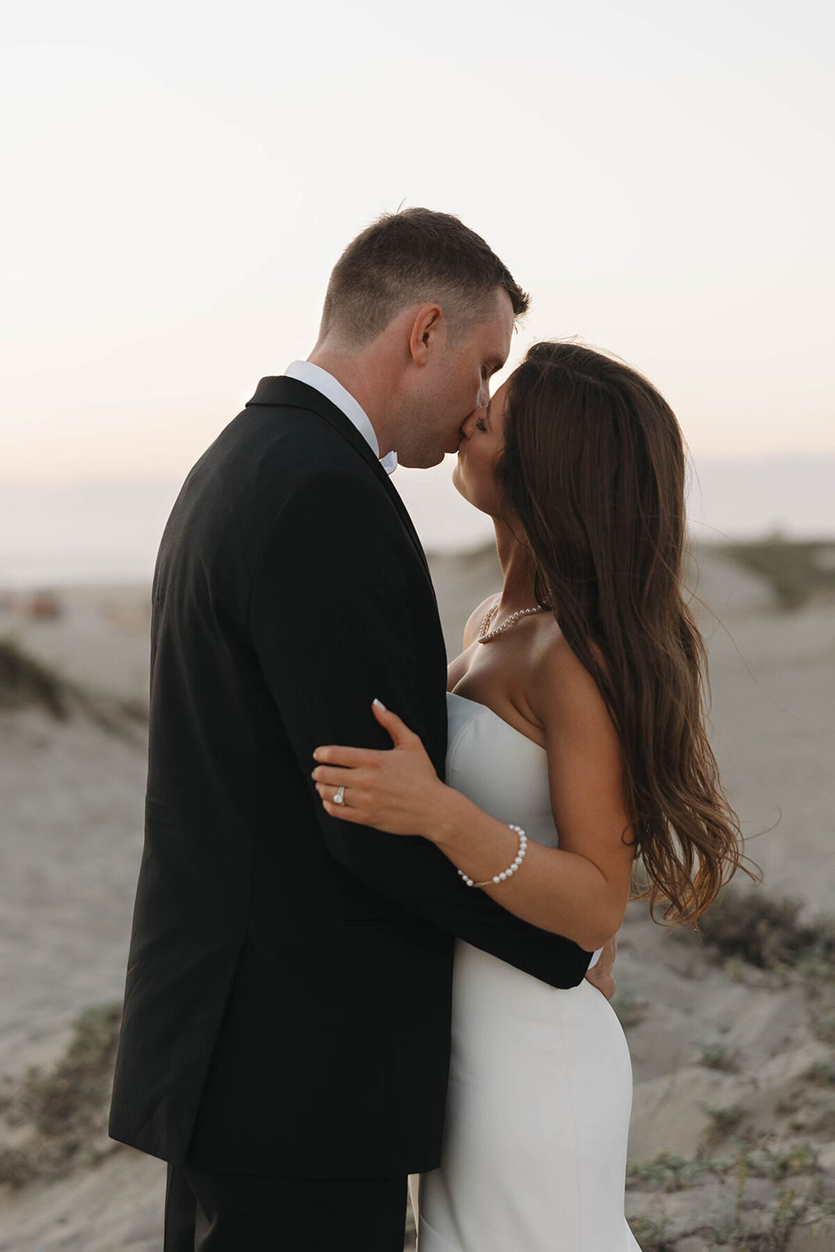 Bride and groom kissing on the beach at dusk