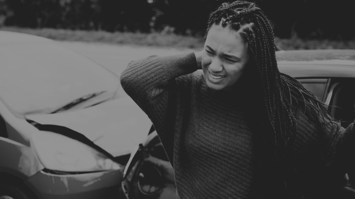 Woman standing in front of car crash holding her neck in pain.