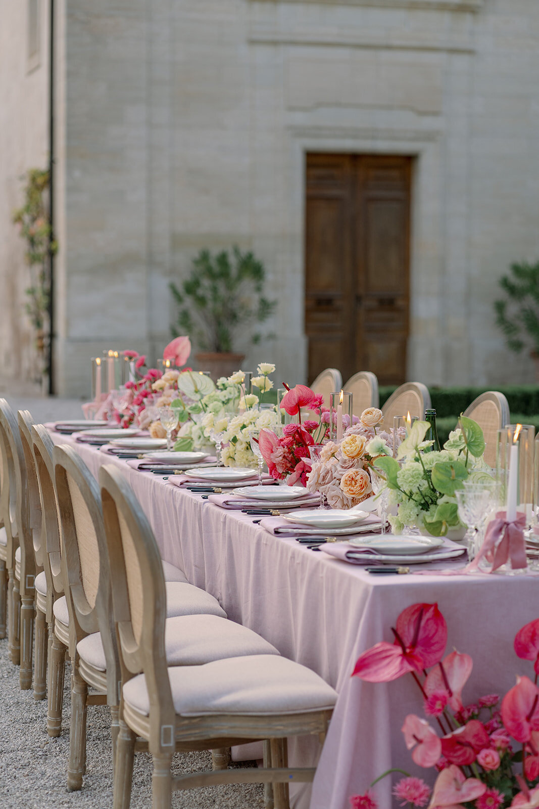 Long wedding reception table with blush linens, pink florals, and crystal glassware at Château de Tourreau.