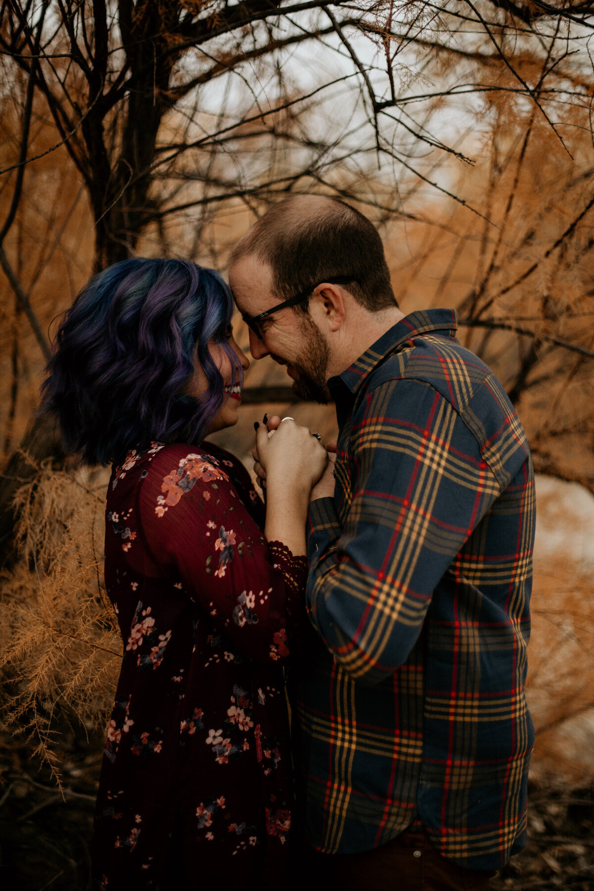 blue haired woman looking into husbands eyes with orange leaves behind them