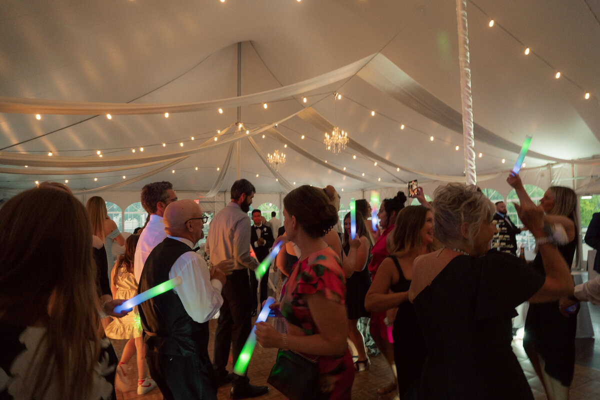 Wedding guests dancing under white tent with string lights and glow sticks