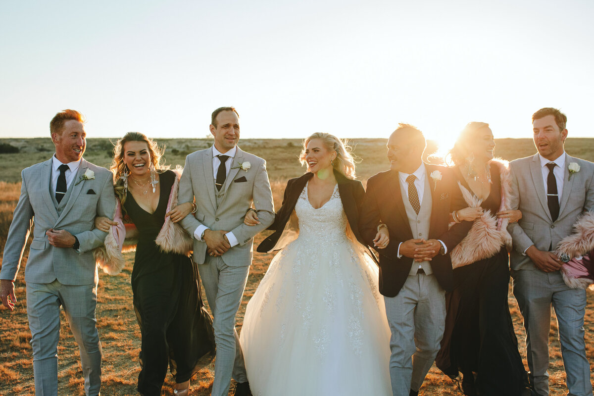Friends in the bridal party walking together with linked arms, sharing laughter at sunset in a natural, candid moment.