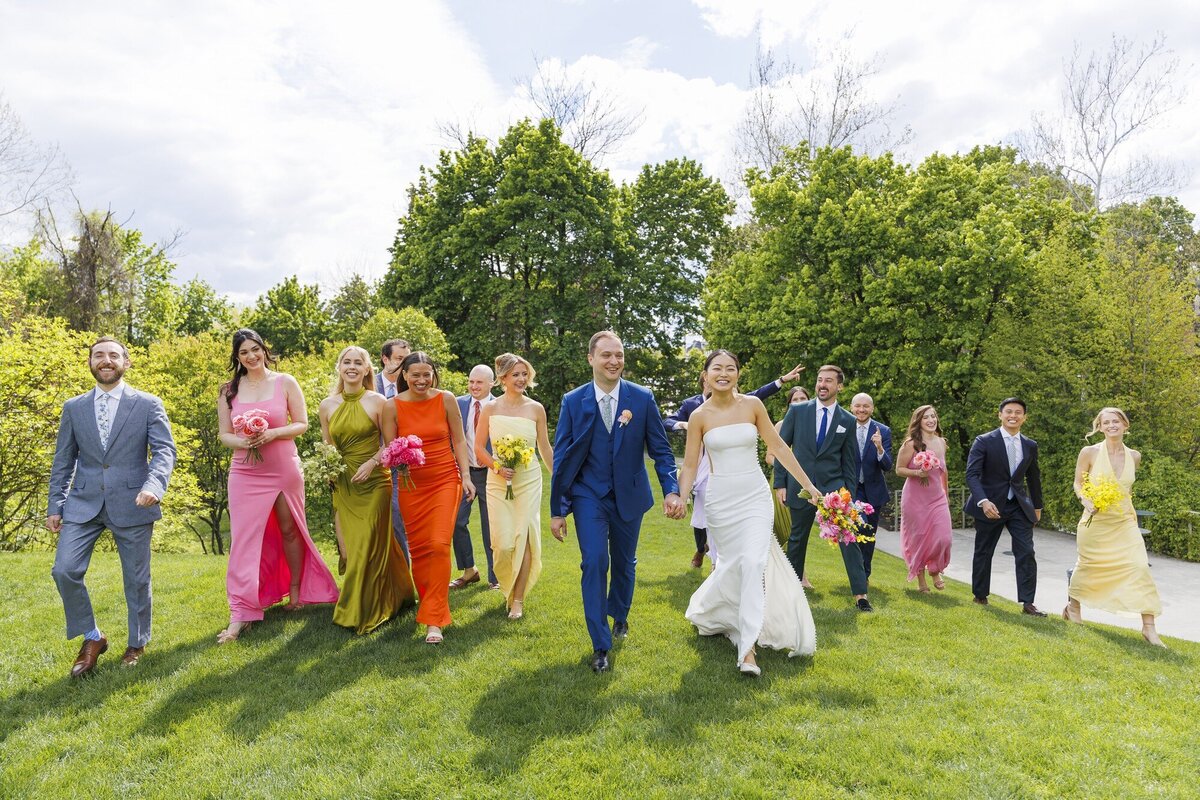 Wedding party in bright colorful outfits walking across a green lawn with the bride and groom