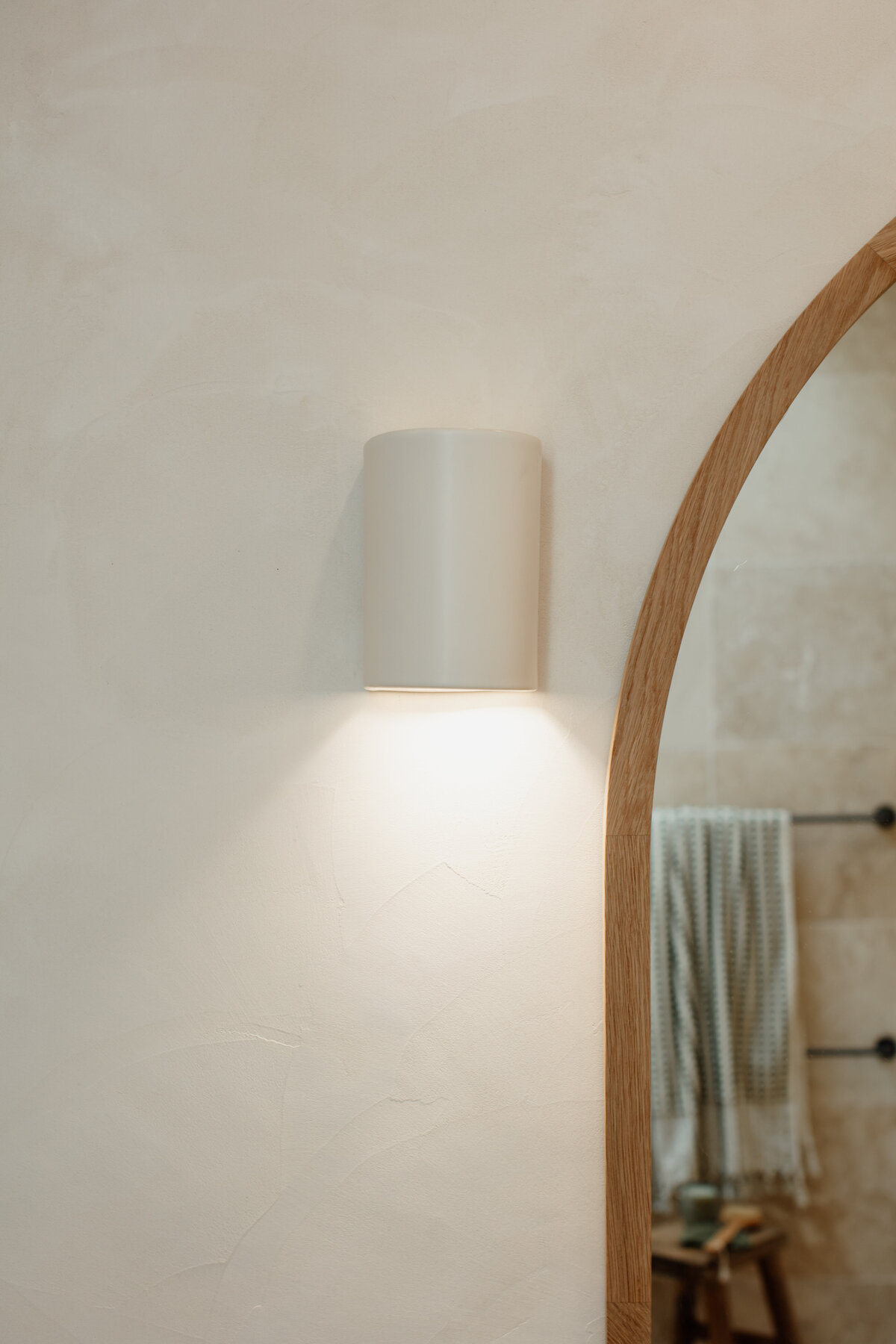 A Newcastle interior designer has crafted a minimalistic room where a wall sconce gently lights up soft textures and a wooden mirror, showcasing the essence of bespoke interior design in Newcastle NSW.