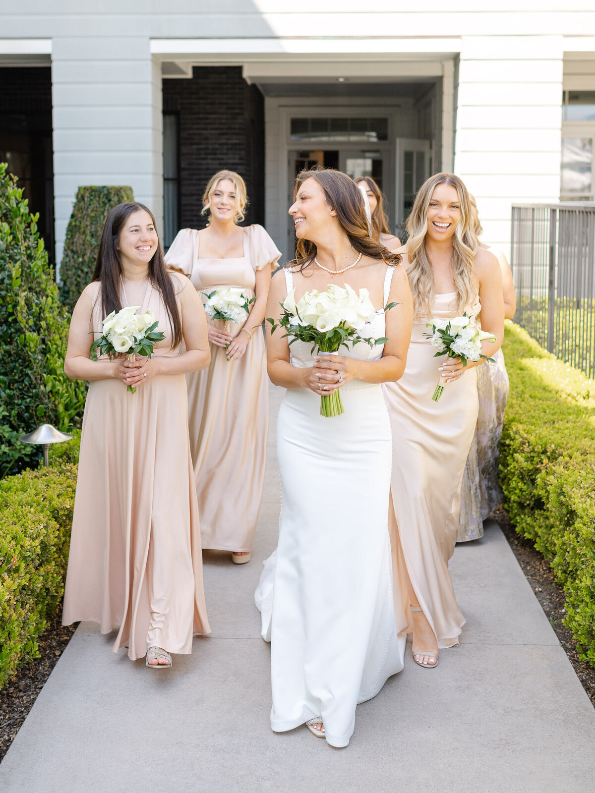 Bride and bridesmaids in champagne dresses holding bouquets, walking at Lido House