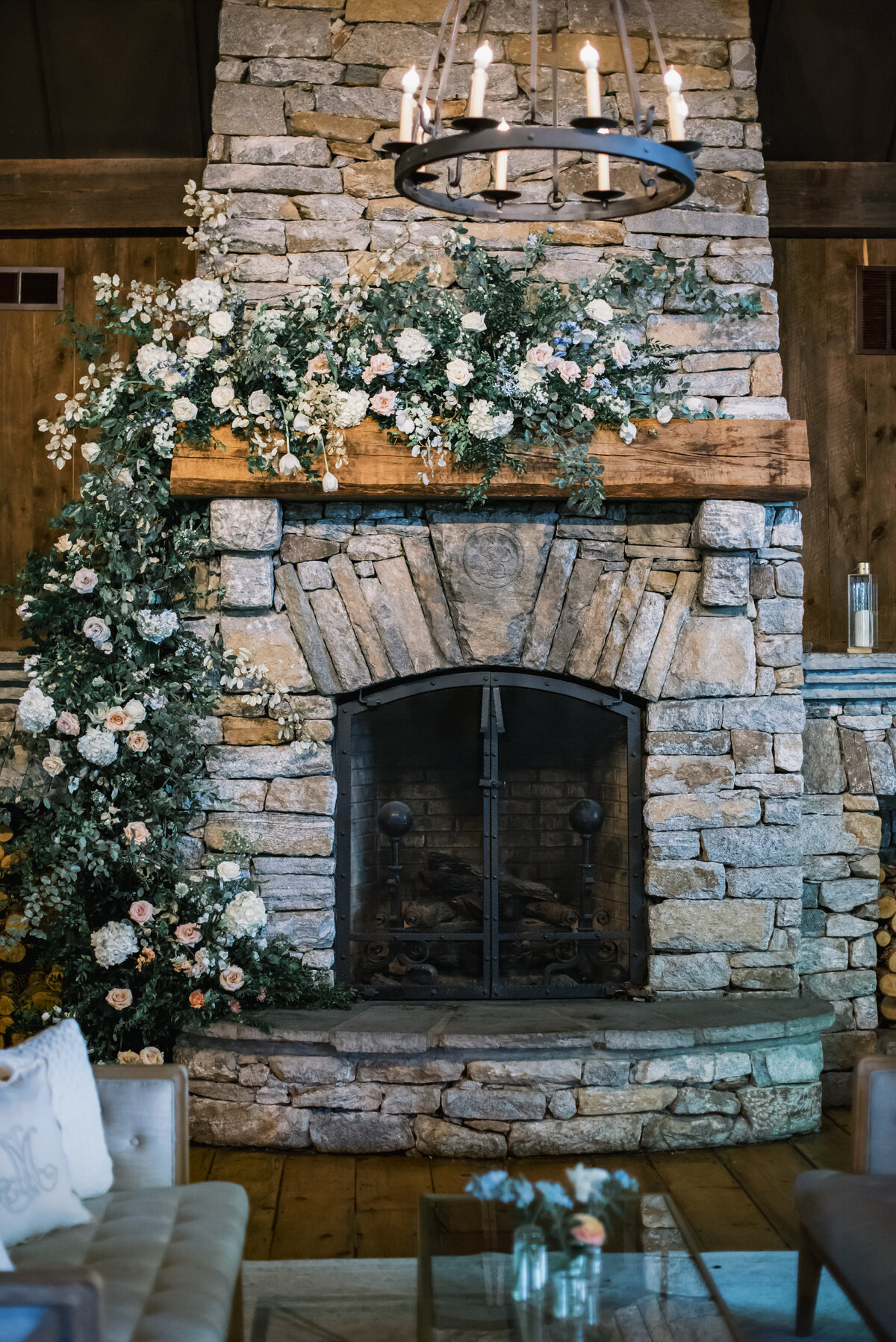 Stone fireplace decorated with lush floral arrangements and soft blue lounge seating during an indoor wedding reception at Old Edwards Inn in Highlands, North Carolina.