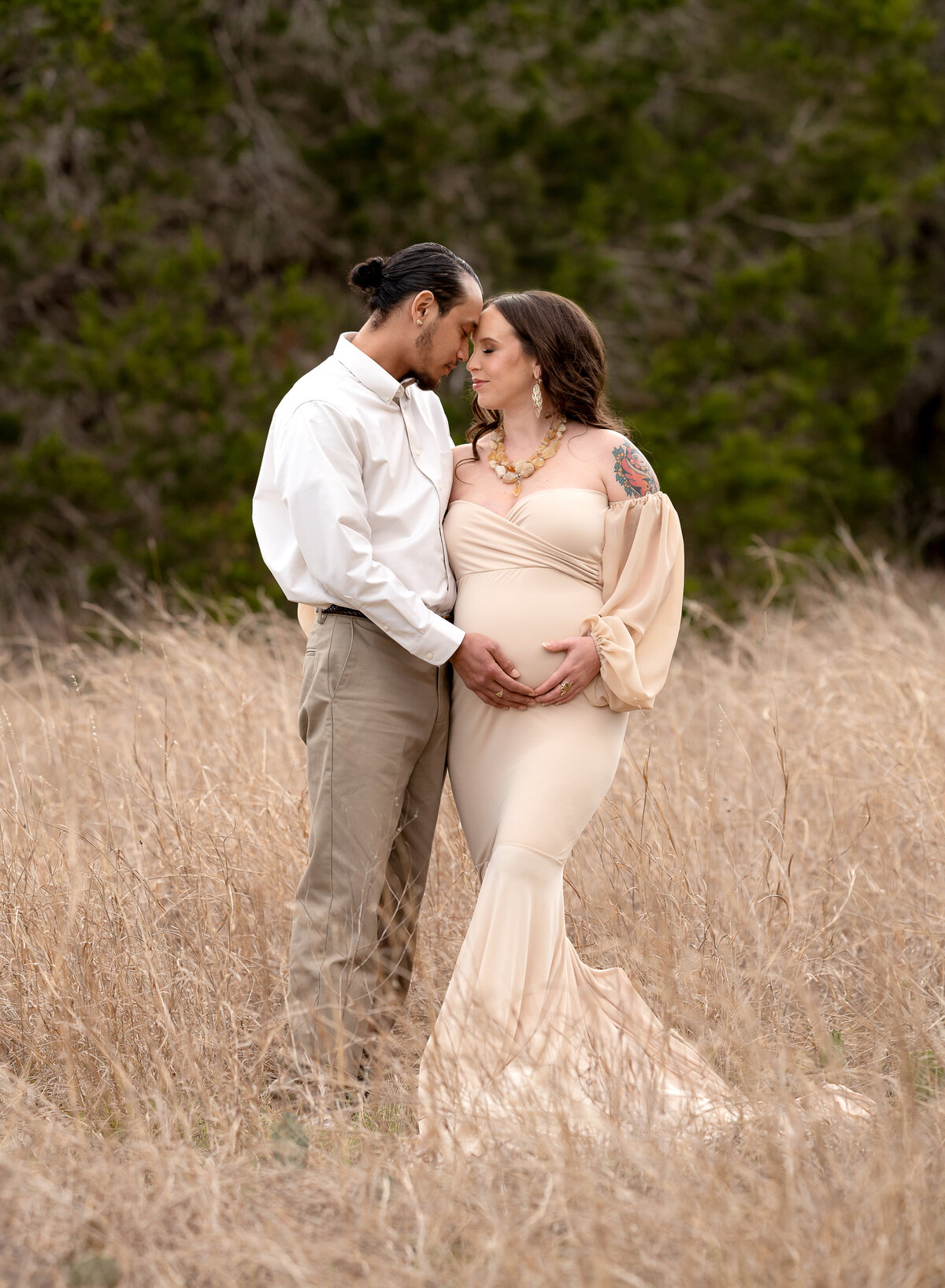 pregnant couple wearing neutral tones in a field