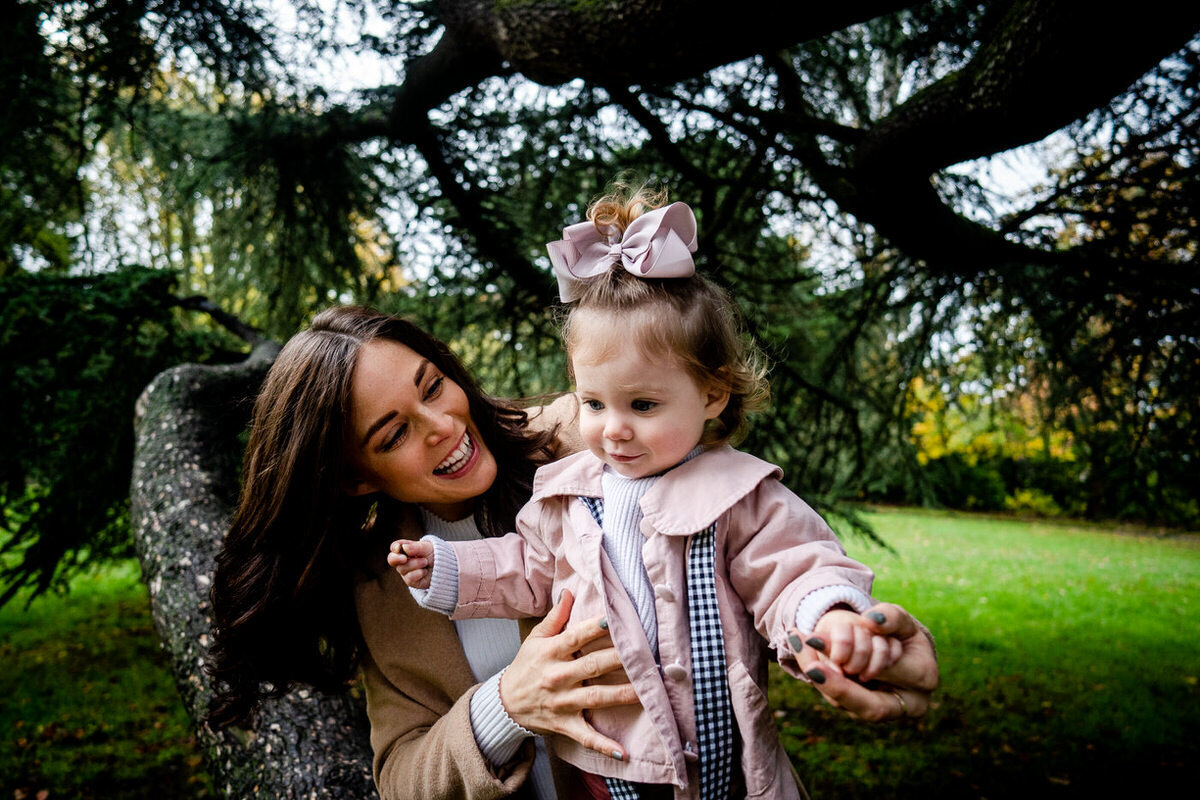 mum looks so happy and daughter walking along branch with pink bow in her hair