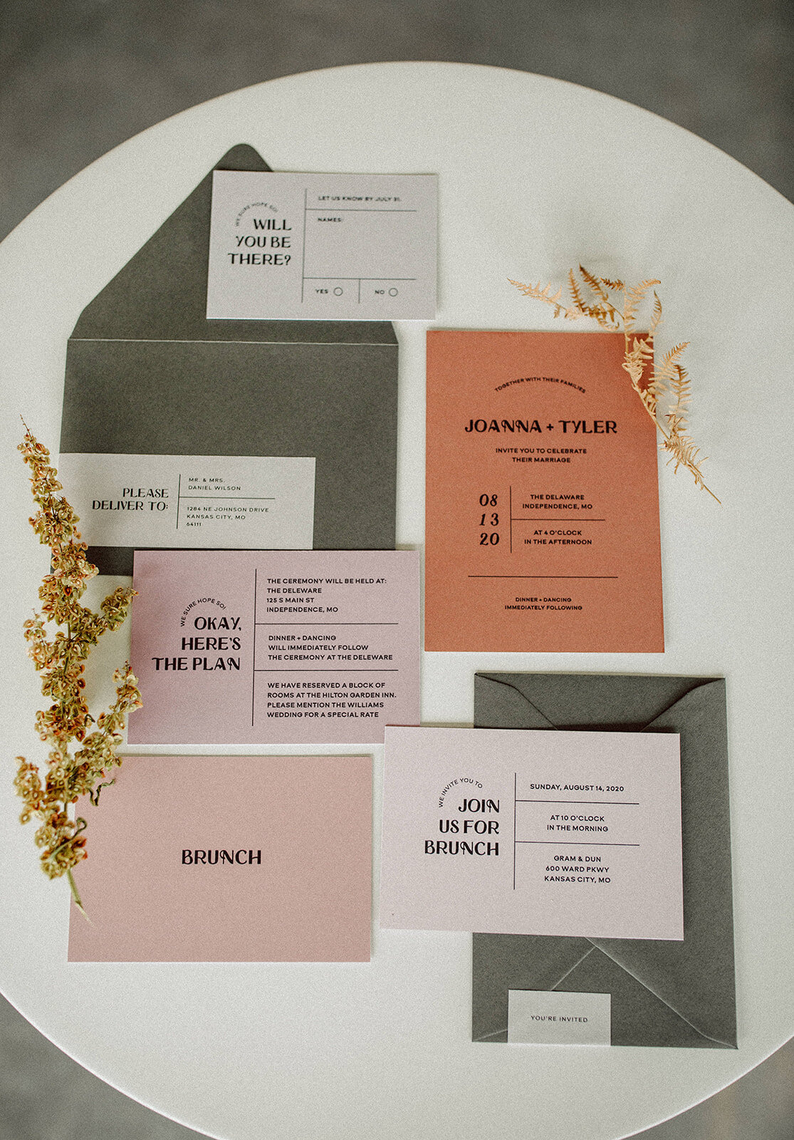 Light gray, peach and mauve-colored wedding stationery with black font atop a white table.