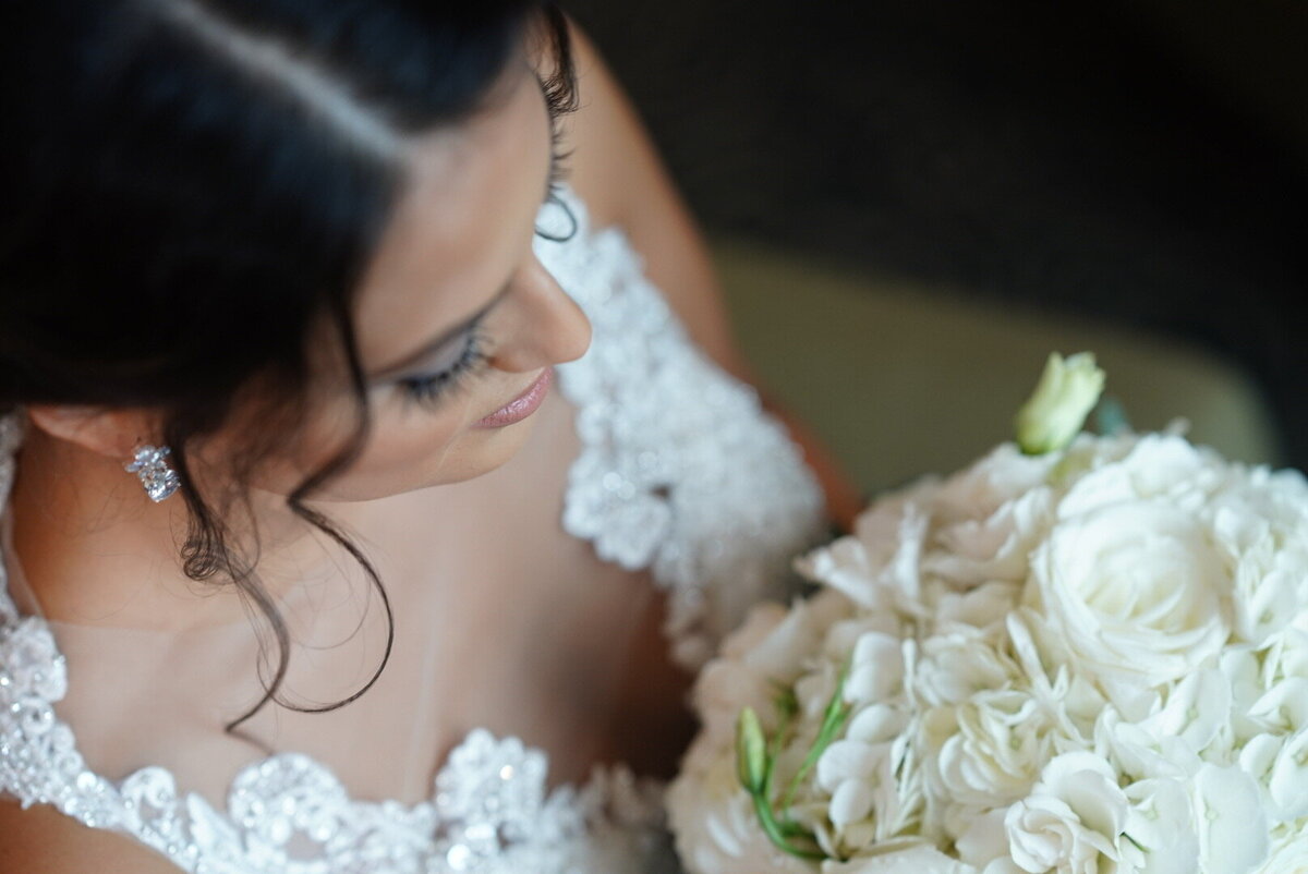 A close-up of a bride admiring her bouquet, capturing her delicate expression and the intricate details of the flowers. This image highlights the beauty and emotional connection of the bridal portrait, showcasing the elegance and personal touch of her wedding day.