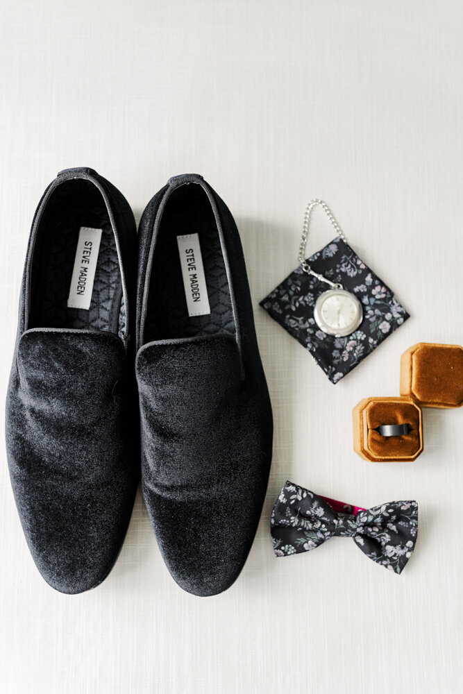 a flat lay of the groom's shoes, watch, bow tie and other wedding details