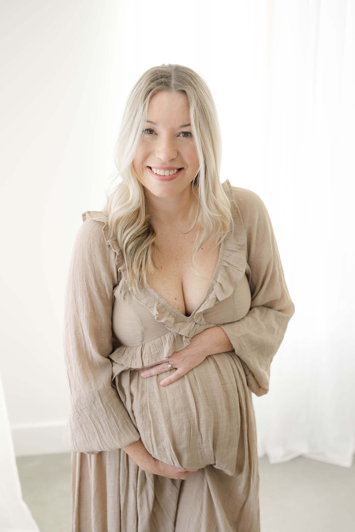 beautiful mother to be smiling in a natural light studio craddling her bump