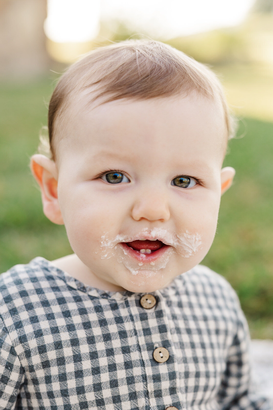 Little boy smiles with frosting on face during one year cake smash