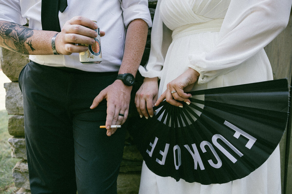 Unique and anti-bride candid ring shot of newly married couple featuring beer, cigarette, rings and a fan.