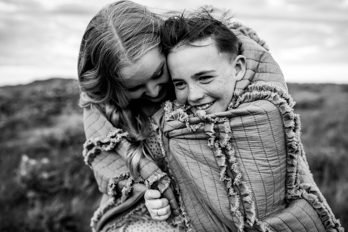 Black and white image of siblings hugging in a blanket  by Portland family photographer.