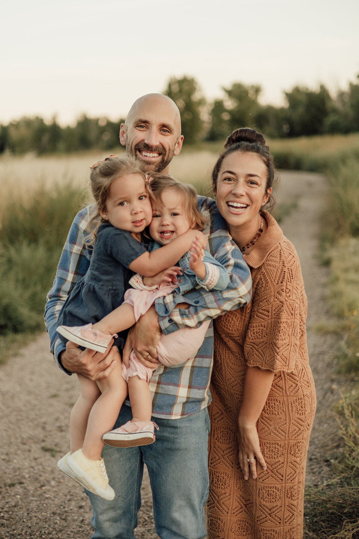 family of four looking at the camera smiling while dad is holding two little girls in longmont colorado