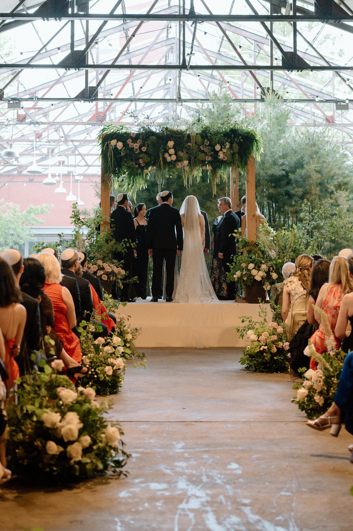 Bride and groom at the altar surrounded by greenery and floral aisle decor.
