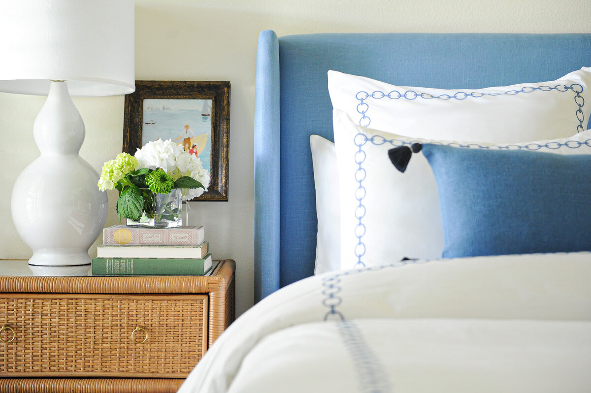Bedroom decor. Blue upholstered headboard, embroidered bedding, and rattan nightstand.