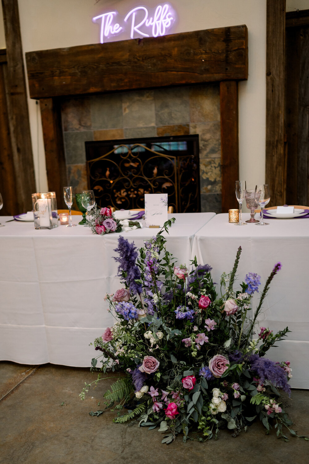 Floor floral arrangement in blush and purple hues placed in front of the head table, with a custom neon name sign above the door, at a Montana summer wedding reception at The Woodlands at Cottonwood Canyon.