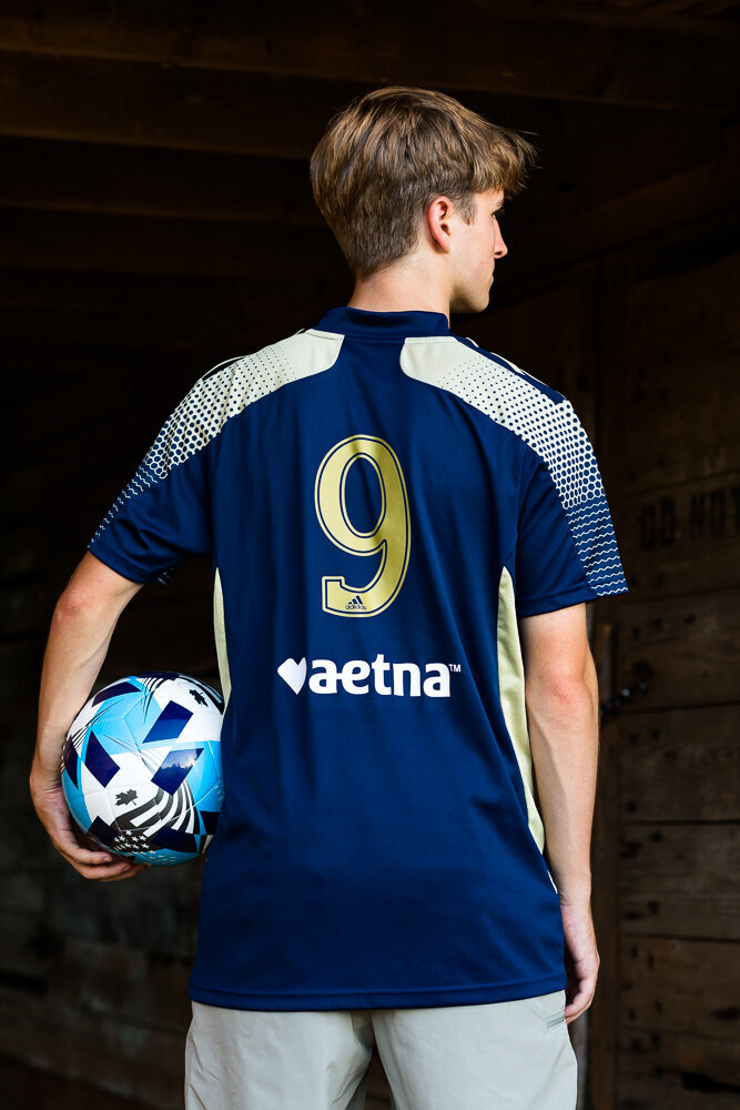 Sports photo session of a soccer player wearing his jersey and holding a soccer ball.