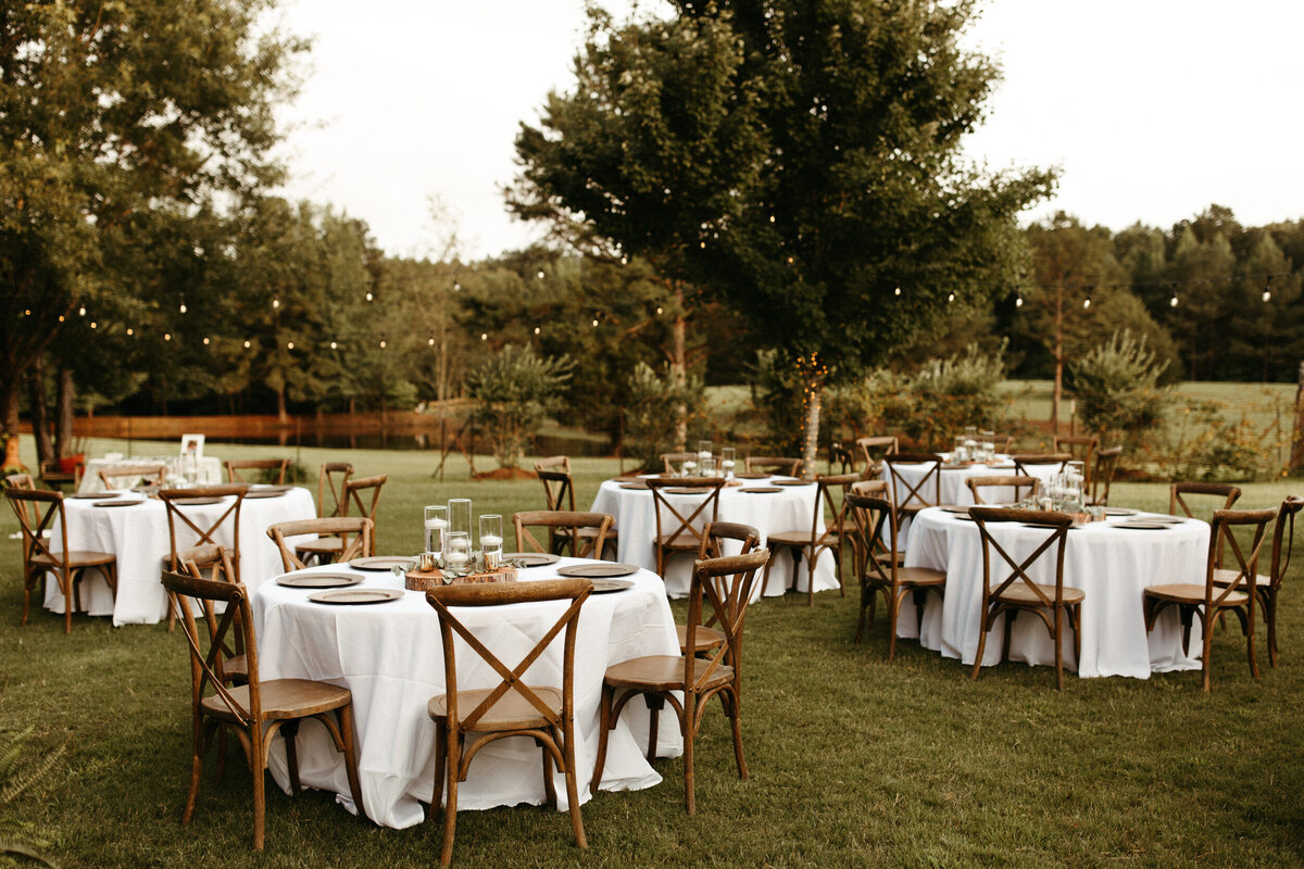 Backyard wedding reception with tables and wooden chairs and string lights