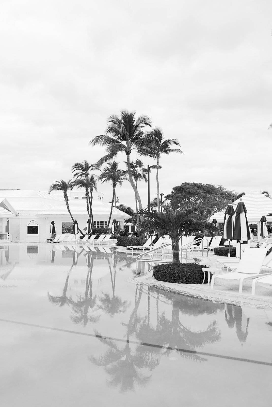 A black-and-white image capturing the calm reflection of palm trees and poolside at the Ocean Reef wedding venue in Key Largo.