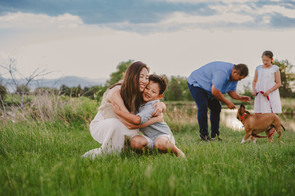 Denver Family Photographer captures mother hugging son while family plays with dog