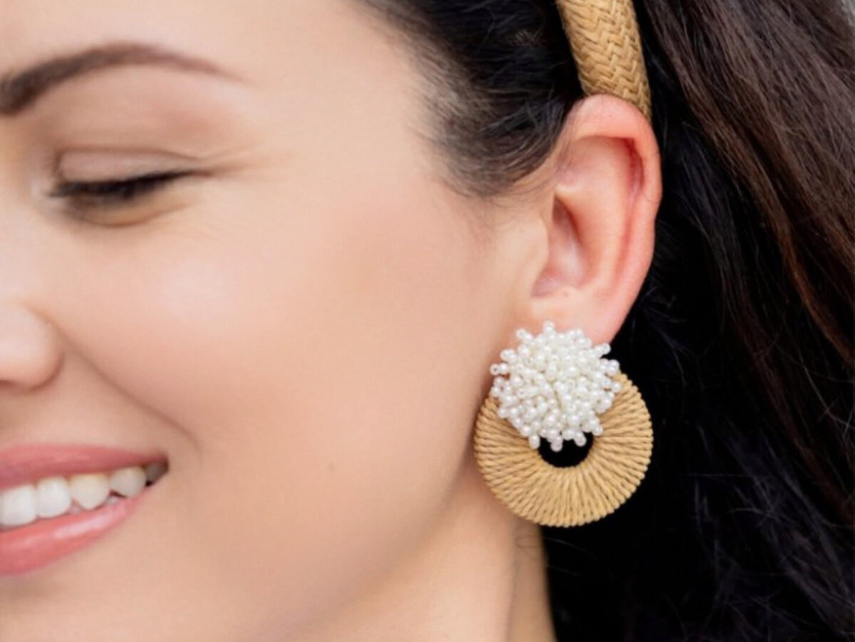 Close-up of a Gaby & Grace earring design with a circular raffia base and pearl cluster center, worn with a natural woven headband.