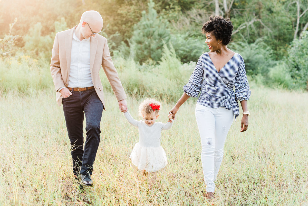 Family walks in a field while holding hands and smiling for a portrait during a Raleigh NC family photography session. Photographed by Raleigh family photographer A.J. Dunlap Photography.