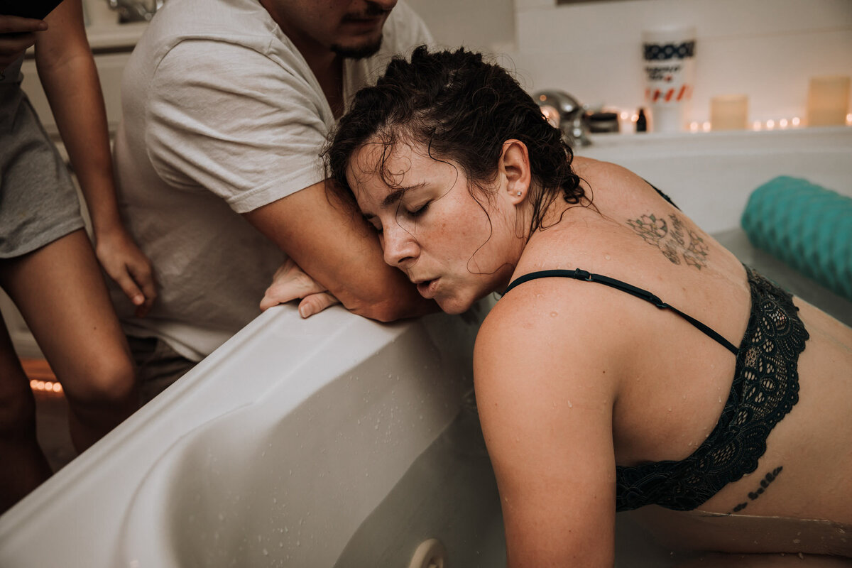 woman leaning on birth tub  while husband supports