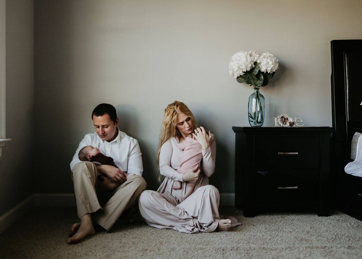 A man and woman, along with their newborn twin girls, pose for a Pittsburgh newborn photographer on the floor.