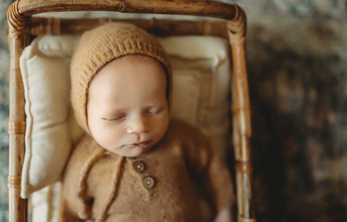baby sleeping in a small crib wearing a brown soft outfit with a hat