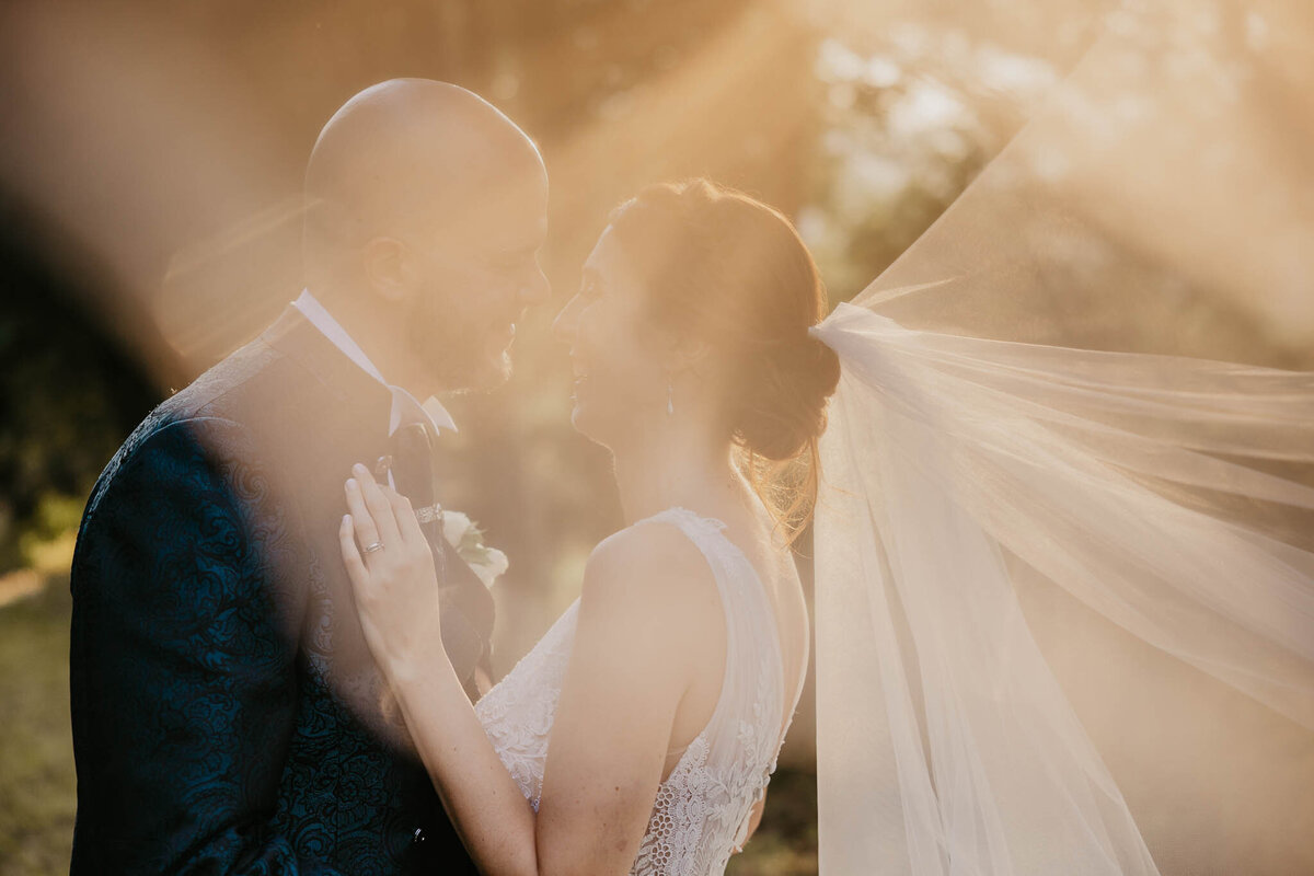 Bride and groom with veil glowing in golden sunset light, villa Bivigliano wedding photographer Tuscany.