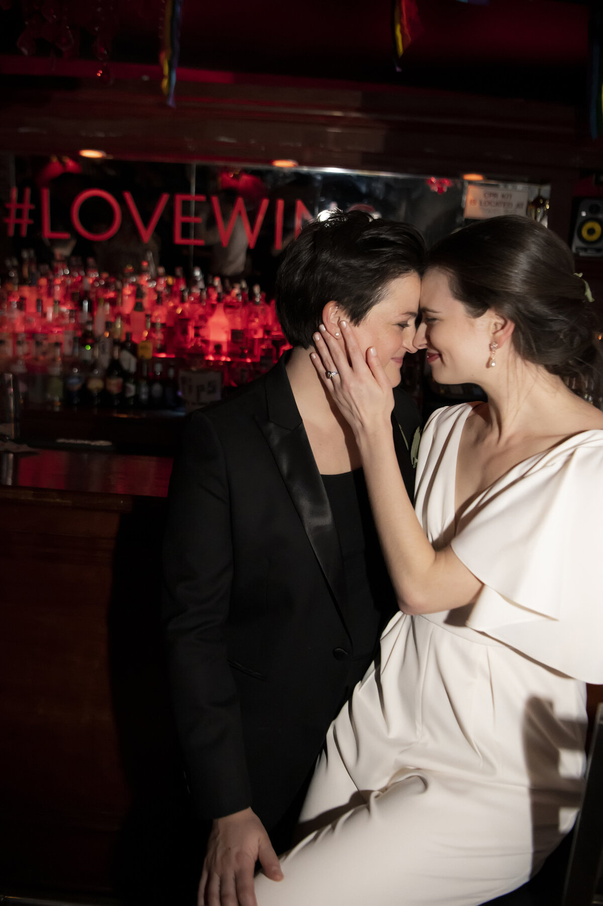 A newlywed couple standing close together with their heads touching while one touches the other's cheek 
