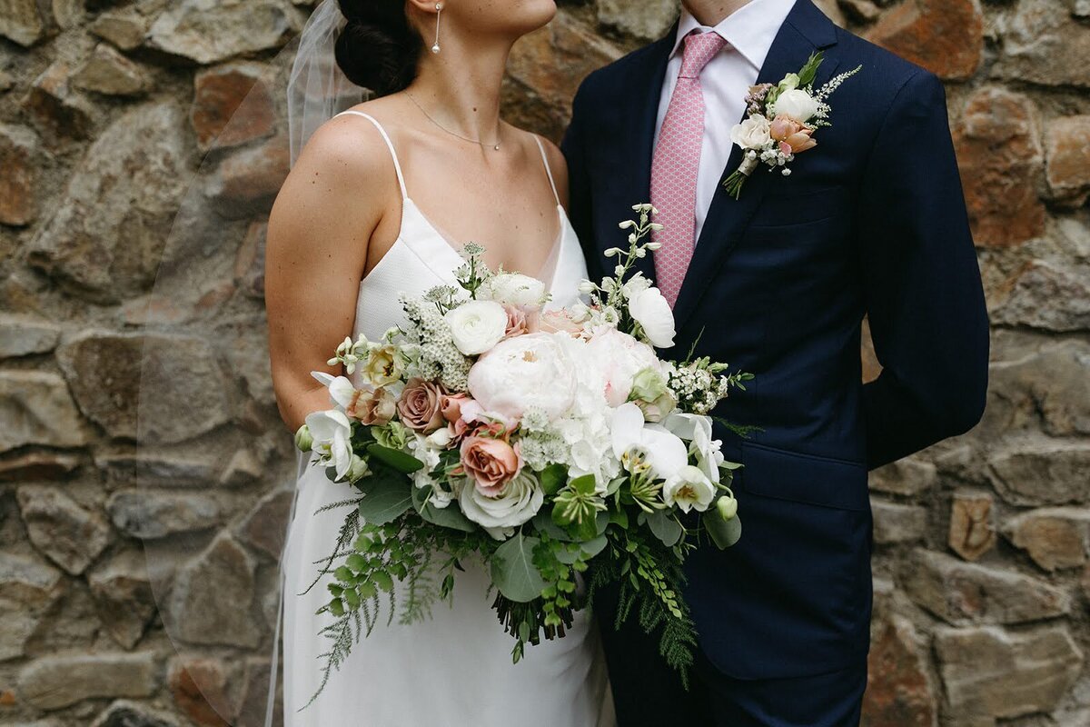 Lush, soft pastel bridal bouquet and boutonniere are focus of faceless bride and groom.