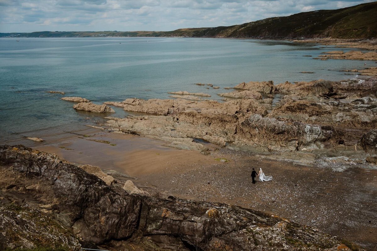 A bride and groom walking along a beach to the sea
