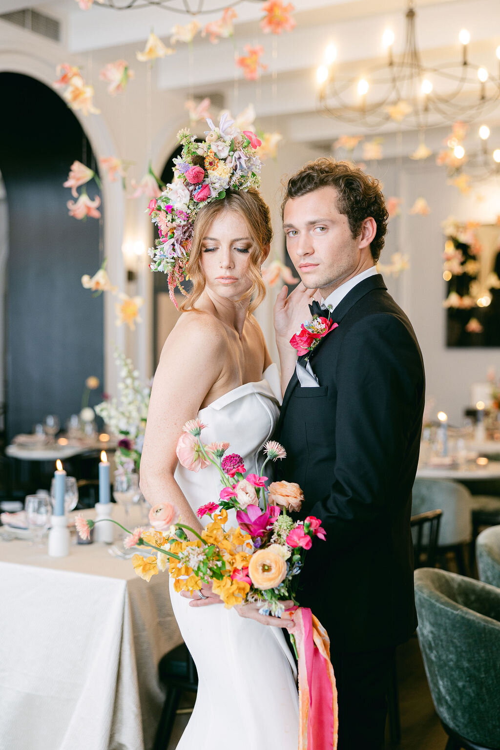 Bride in a sculptural white gown and floral headpiece stands beside her groom amid a vibrant reception setup at The Mills House Hotel, Charleston—captured by luxury wedding photographer Amia Marcell.