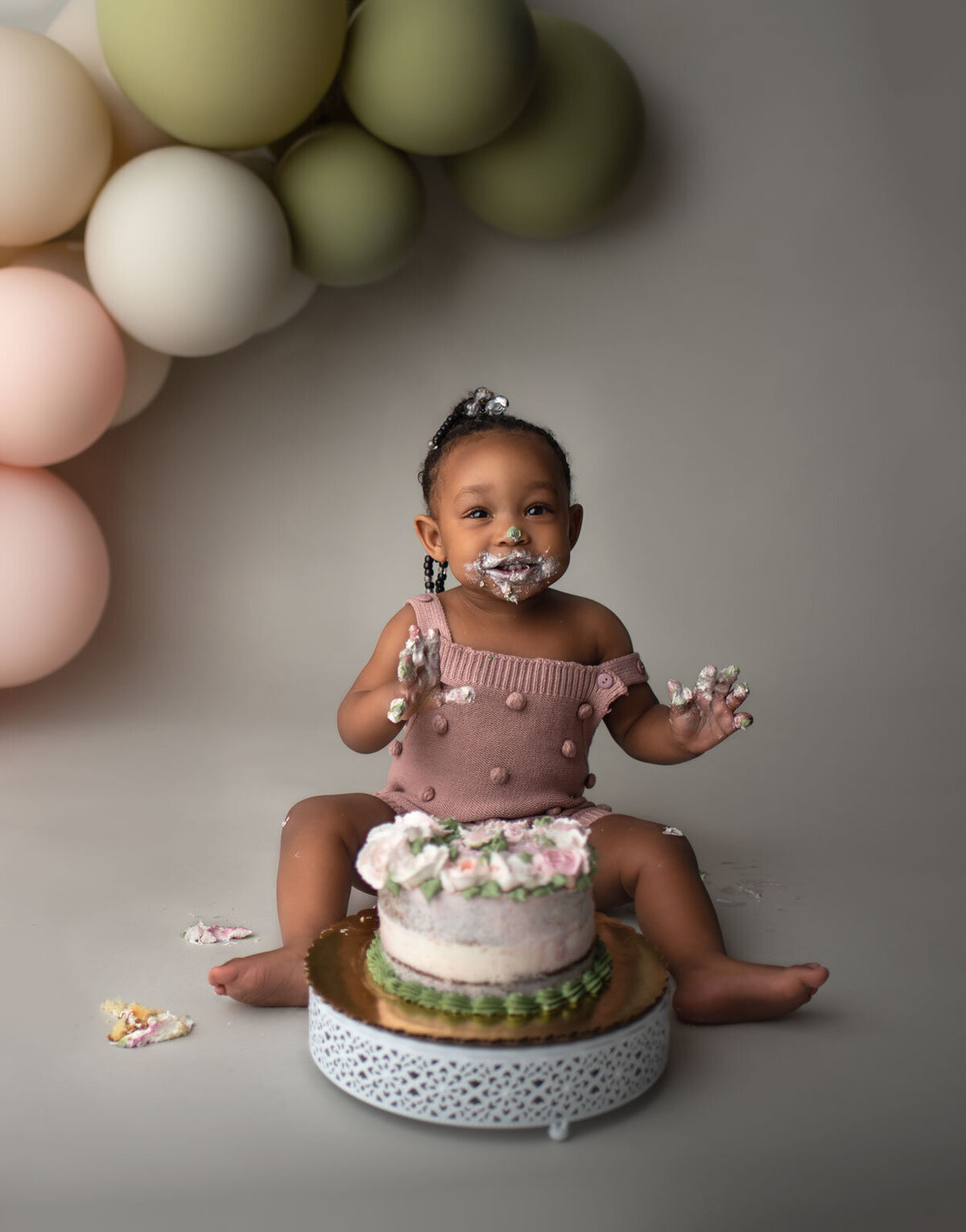 happy baby eating cake with balloons behind her