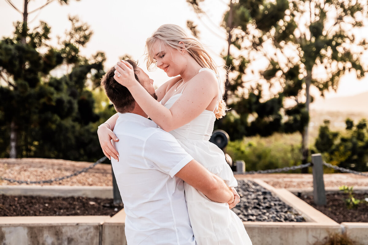 man lifting up fiance into an embrace as the woman brushes the hair off his face - Townsville Engagement Photography by Jamie Simmons