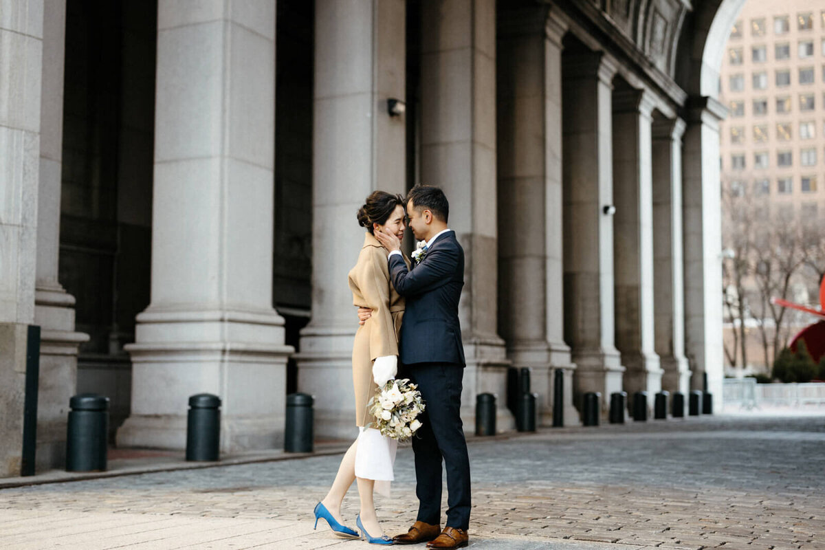 The groom is touching the bride's face in front of an old building with columns.