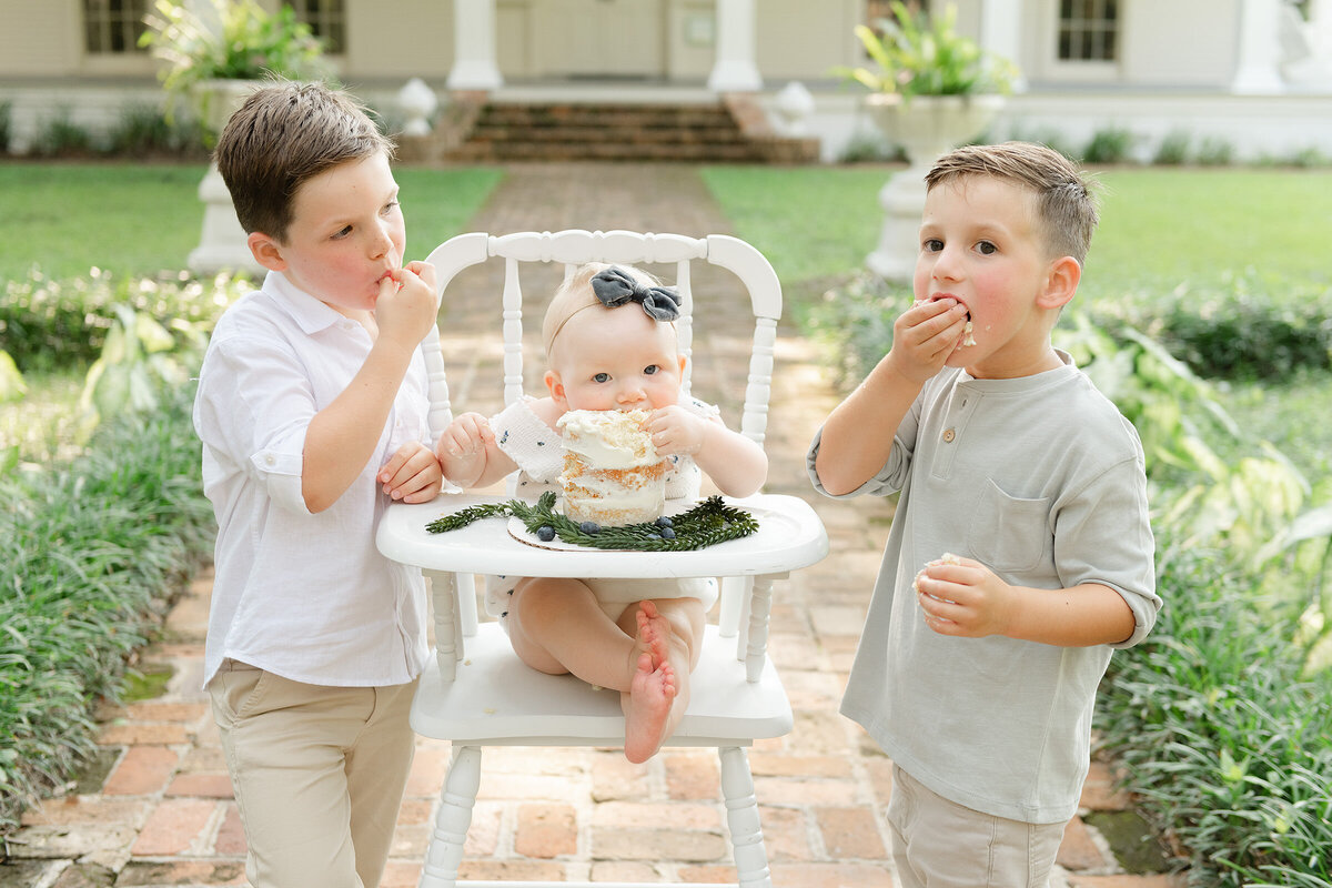Three children eating smash cake in a high chair for a photoshoot with a Destin family photographer.