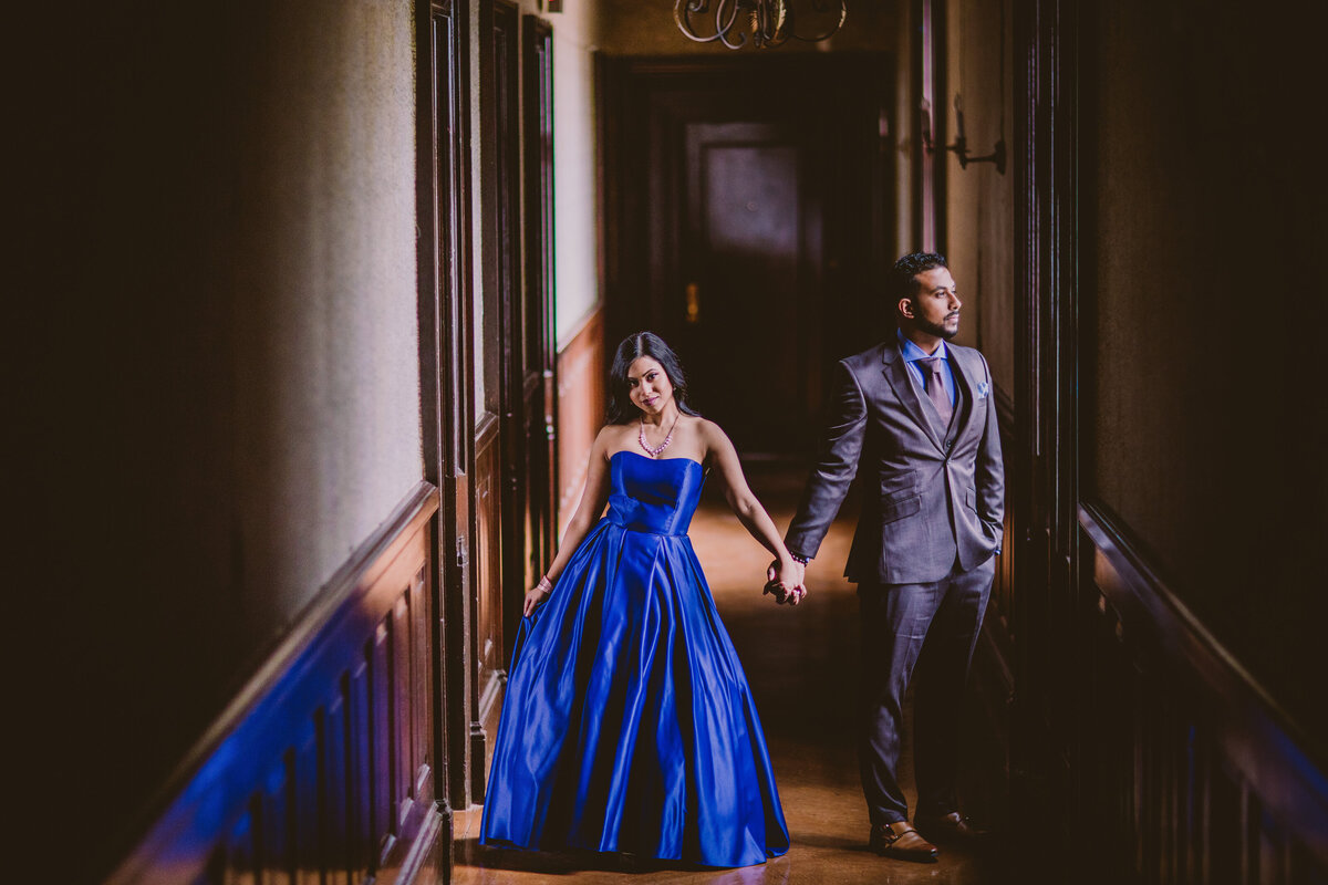 An engaged couple in blue outfits posing inside a hallway at the hempstead house in sands point preserve