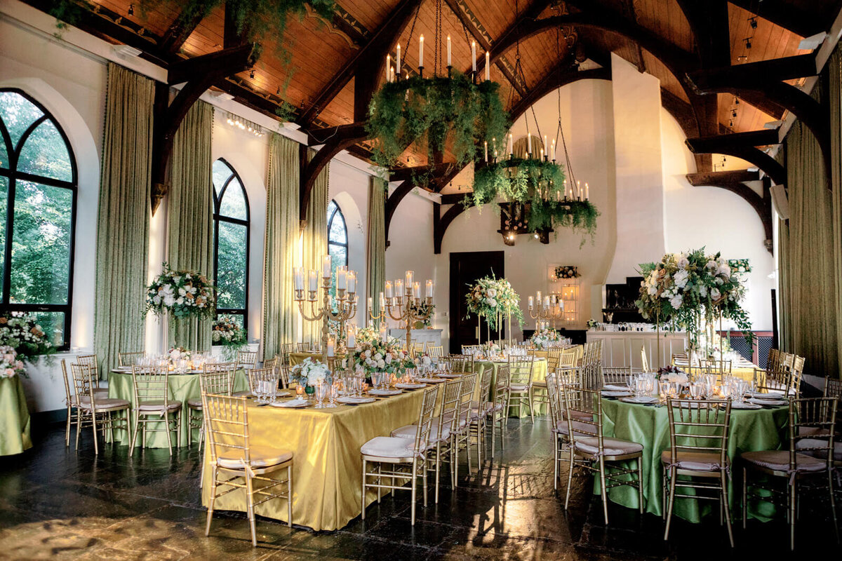 Elegant wedding reception room with candle chandeliers, bronze tables and chairs with large flower bouquet and candle centerpieces