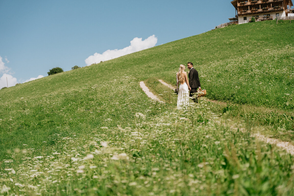 Bride and groom walking through meadow in Val di Funes