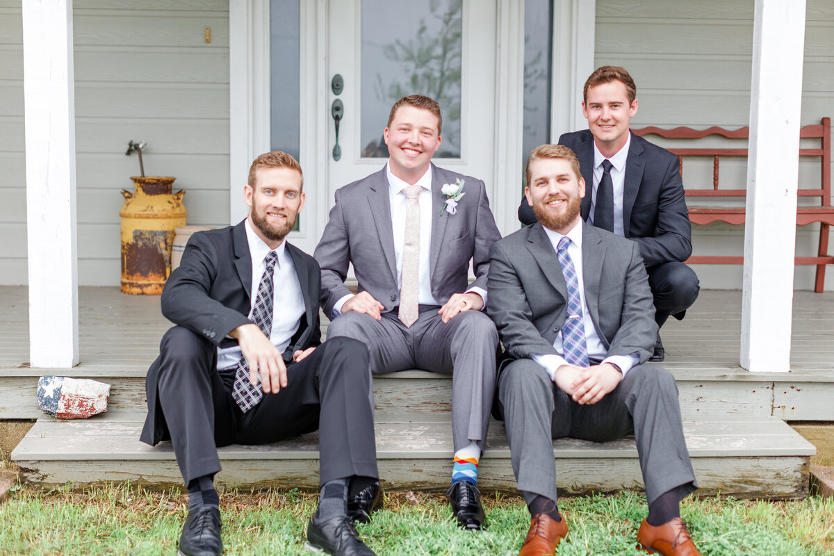 groomsmen sit together in suits on porch of wedding near Austin Texas