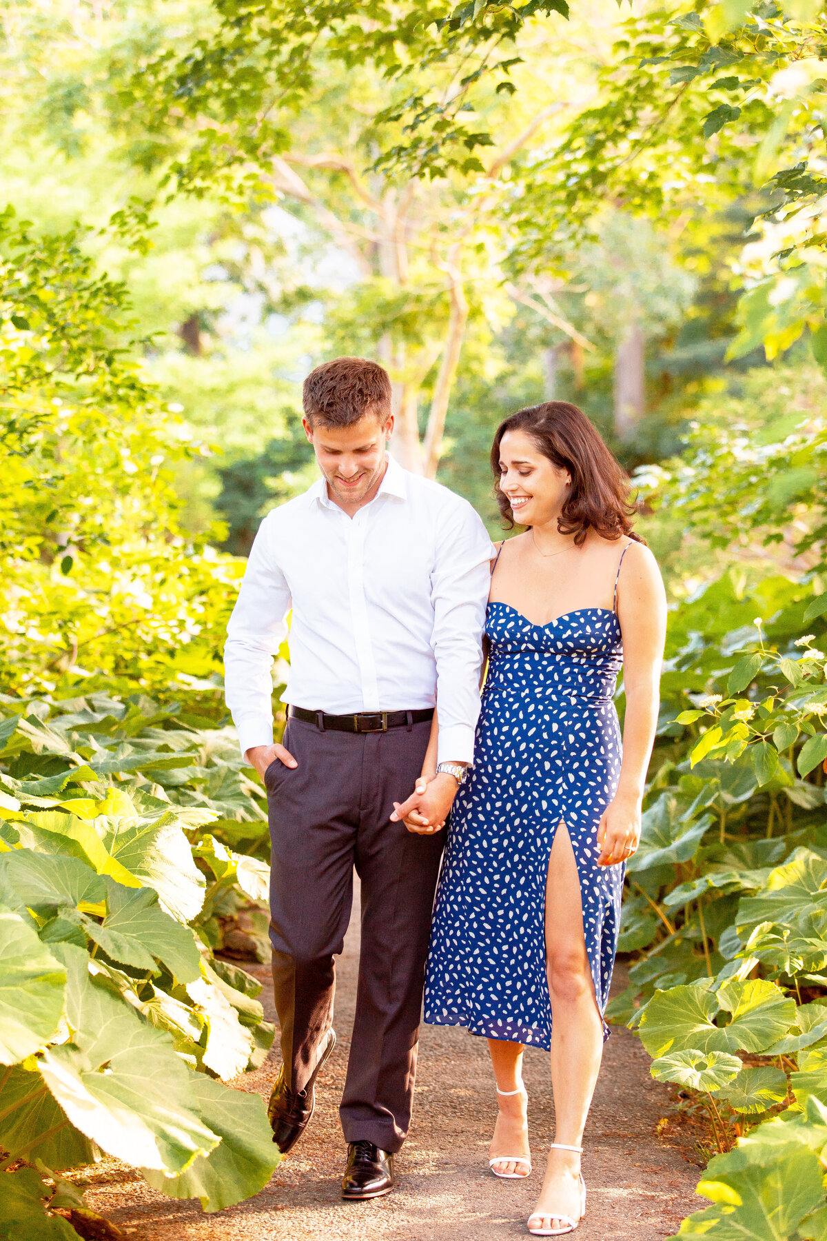 Couple hold hands and walk through a garden.